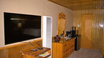 Quarto com televisão de tela plana na parede, cômoda de madeira com gavetas, espelho e cafeteira.