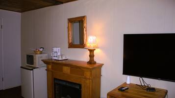 A room with a fireplace, a television mounted on the wall, a microwave, and a small table with a lamp.