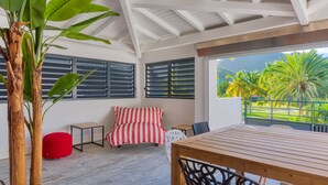 A room with a wooden table, a red and white striped sofa, a red bean bag, and a large window with a view of palm trees. - One bedroom loft marina Anse Marcel (Cul-de-Sac)