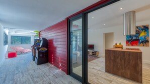 A modern living room with a red wall, a gaming console, a wooden reception desk, and a large window. - One bedroom loft marina Anse Marcel (Cul-de-Sac)