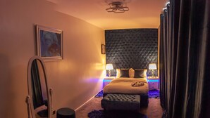 Ein Schlafzimmer mit einem großen Bett, zwei Nachttischen mit Lampen, einer Kopfteil, einem Spiegel und einem gerahmten Bild an der Wand.