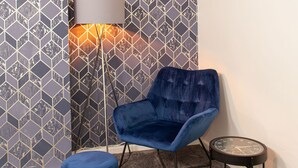 Ein Zimmer mit gestreiftem Wandpapier, einem blauen Sessel, einem kleinen runden Tisch und einer Stehlampe.