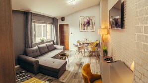 A modern living room with a grey sectional sofa, a dining area with yellow chairs, and a brick wall. - Impeccable 1-Bed Apartment in Birmingham (Birmingham)