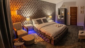 A bedroom with a tufted headboard, a bed with a white comforter, a nightstand with lamps, a striped chair, a small ottoman, and a wardrobe. - Impeccable 1-Bed Apartment in Birmingham (Birmingham)