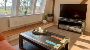 Una sala de estar con televisor, una mesa de centro y una ventana con vistas a árboles.