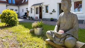 Una estatua de una figura sentada en un jardín, con un edificio al fondo.