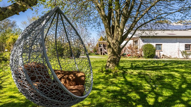 Een hangstoel in een tuin, met een huis op de achtergrond.