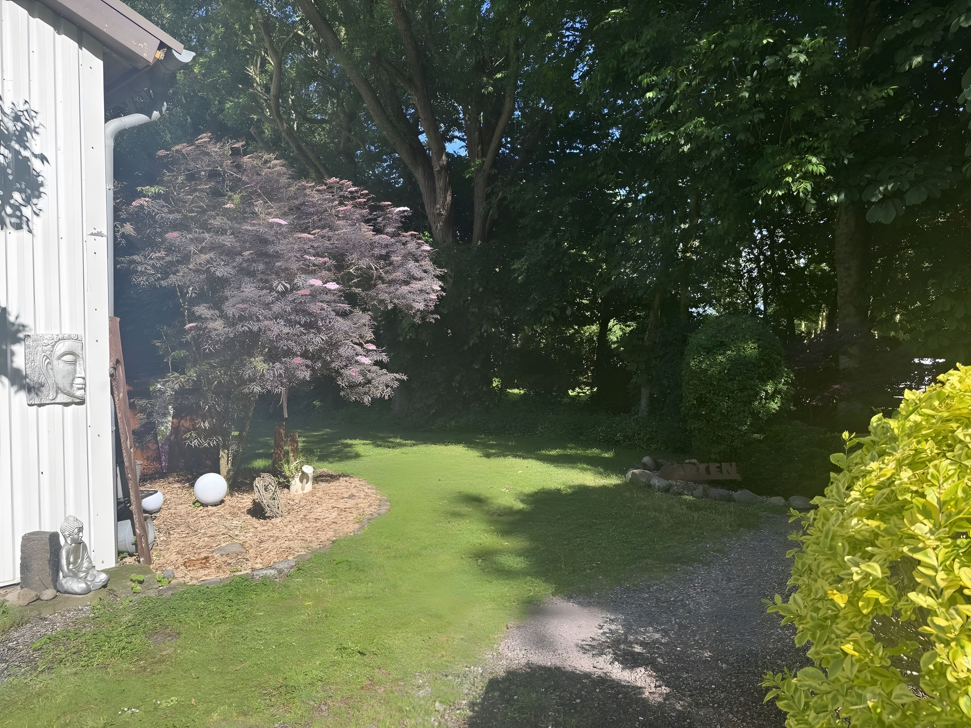 Een tuin met een grindpad, een beeld en een gebouw met een metalen deur.