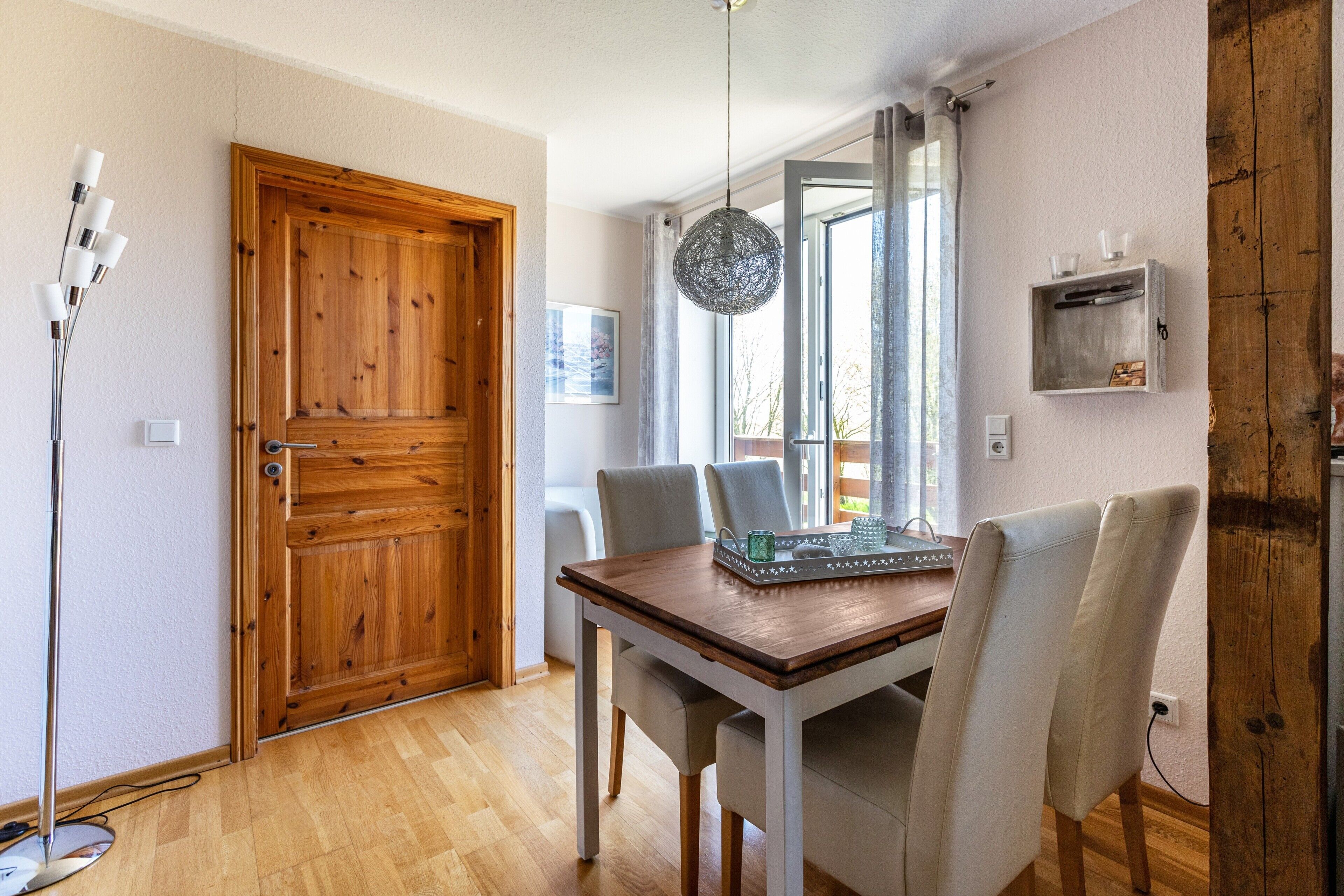 Een eethoek met een houten tafel, stoelen, een hanglamp en een deur.
