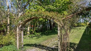 Una pèrgola de fusta amb plantes enfilades, envoltada per una zona verda i arbres.