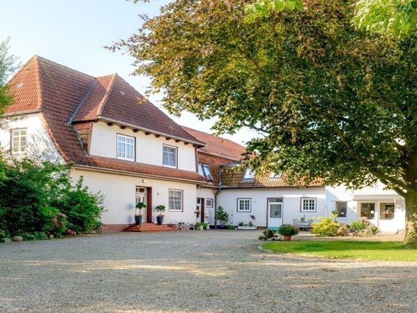A two-story house with a gravel driveway, a front porch, and a tree in the foreground. - Haevn by the Sea Retreat, Apartment Rosenquarz (Reußenköge)