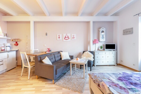 A modern living room with a sofa, a dining table, a TV, and a kitchen area. - Haevn by the Sea Retreat, Apartment Rosenquarz (Reußenköge)