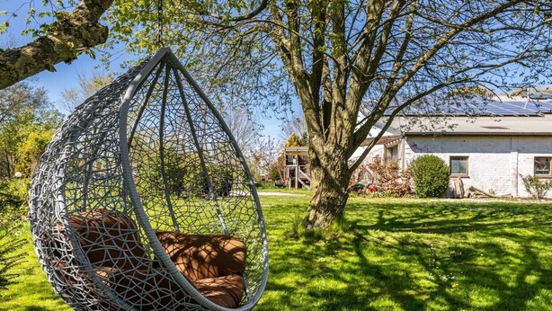 Una silla colgante en un jardín, con una casa al fondo.