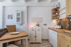 A compact kitchen with a dining table, a cabinet, a coffee machine, and a dishwasher.