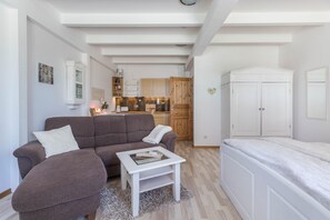 A modern living room with a sofa, a small table, a bed, and a kitchen in the background.