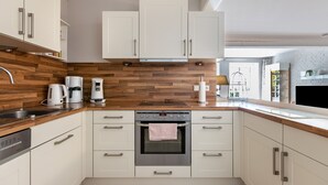Una cocina moderna con armarios blancos, protector de salpicadero de madera, electrodomésticos de acero inoxidable y horno empotrado.