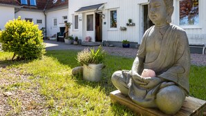 Una estatua de una figura sentada en un jardín, con un edificio al fondo.