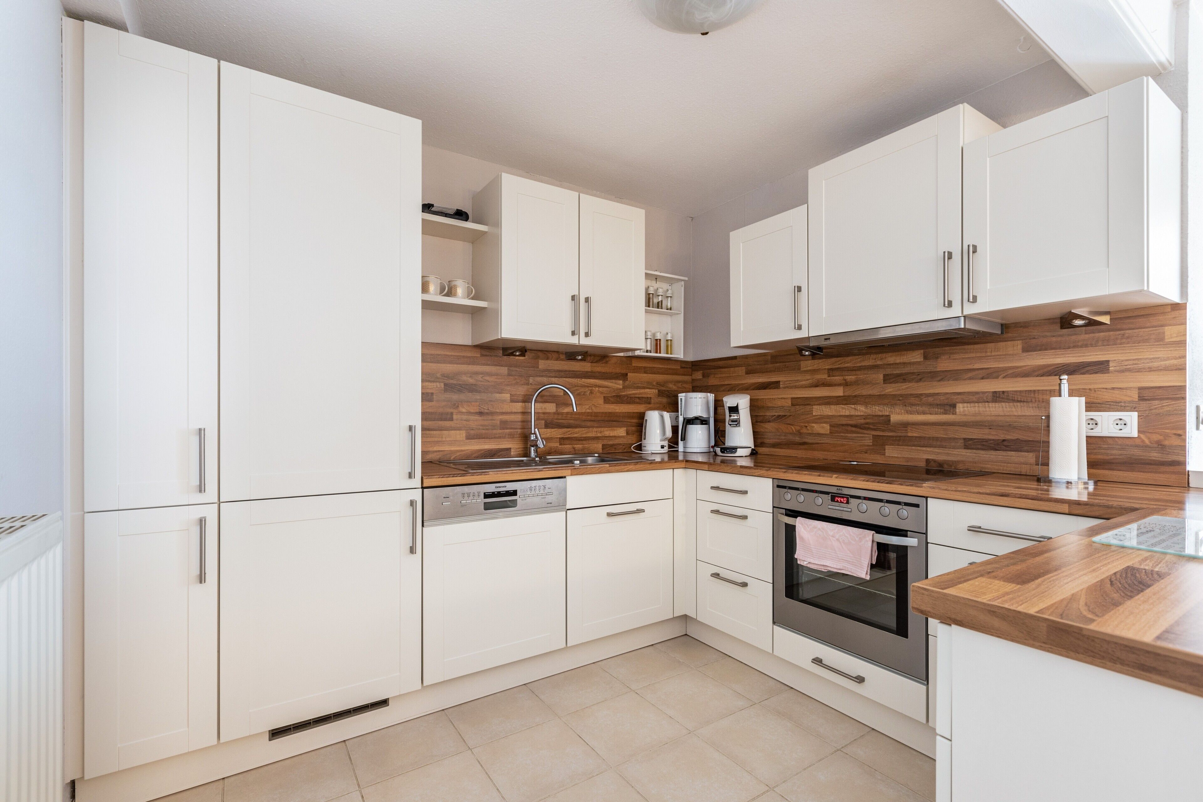 A modern kitchen with white cabinetry, a wooden backsplash, a stainless steel range hood, and a built-in oven.