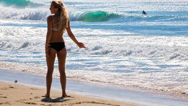 A beach scene with waves, a pier, and a person standing on the sand.