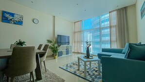 A modern living room with a dining area, a sofa, a TV, and a large window with curtains.