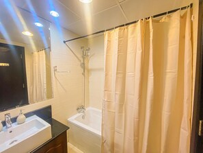 Un baño con una bañera blanca, una ducha con cortina, un lavamanos con espejo y un perchero para toallas.