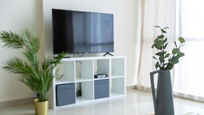 A modern living room with a flat-screen TV, a white entertainment unit, a potted plant, and a vase with a plant.