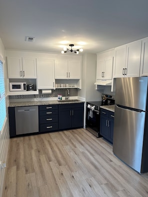 A modern kitchen with white cabinets, a stainless steel refrigerator, a microwave, and a dishwasher.