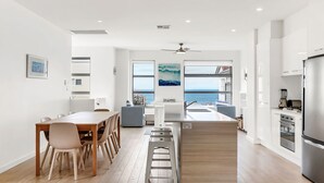 A modern kitchen with a view of the sea, wooden flooring, and a dining area with chairs. - Stunning Sea Views in Excellent Location (Victor Harbor)