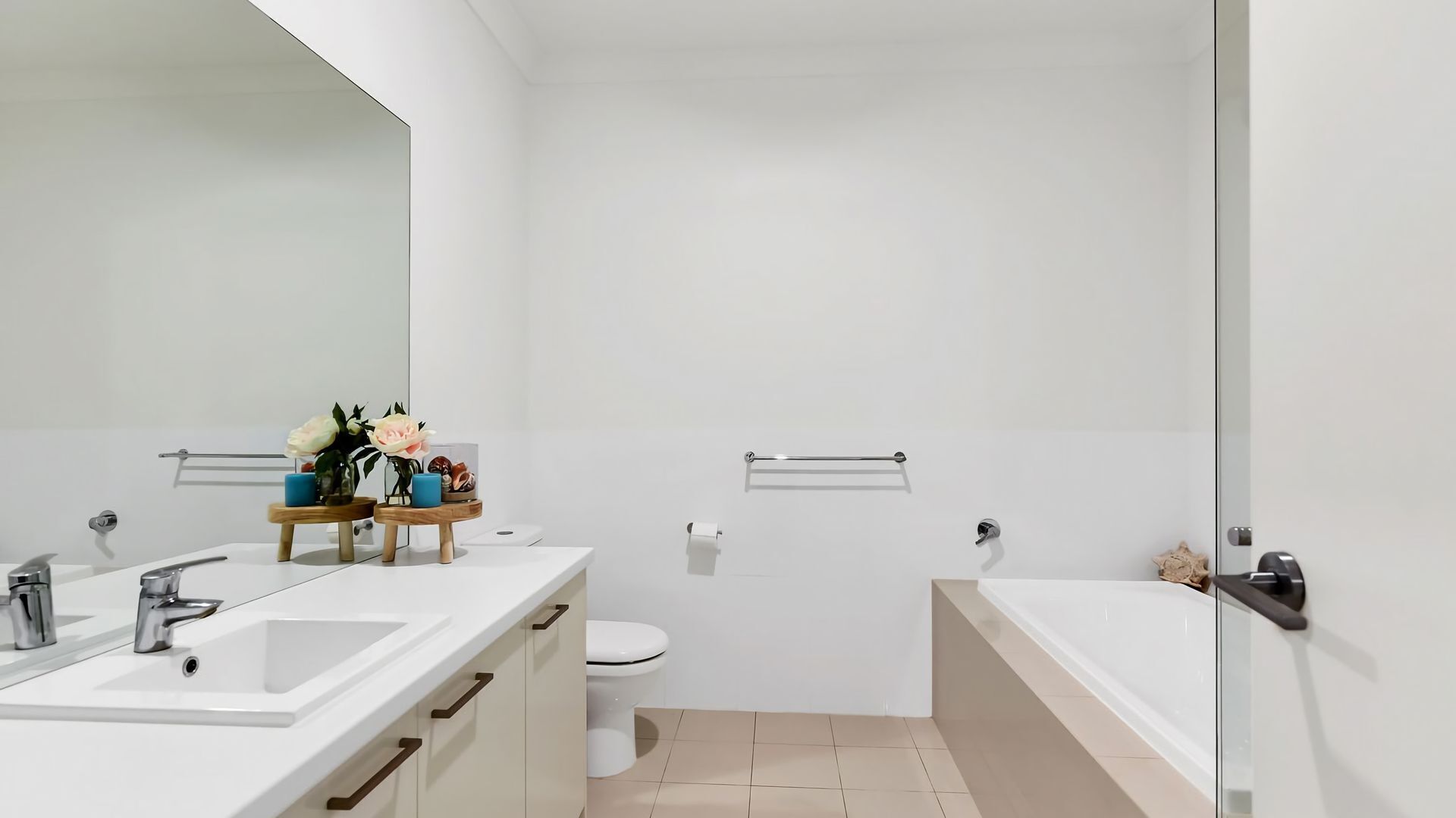 A modern bathroom with a large mirror, a sink with a faucet, a toilet, and a bathtub. There are wooden shelves with decorative items and a towel rack on the wall.