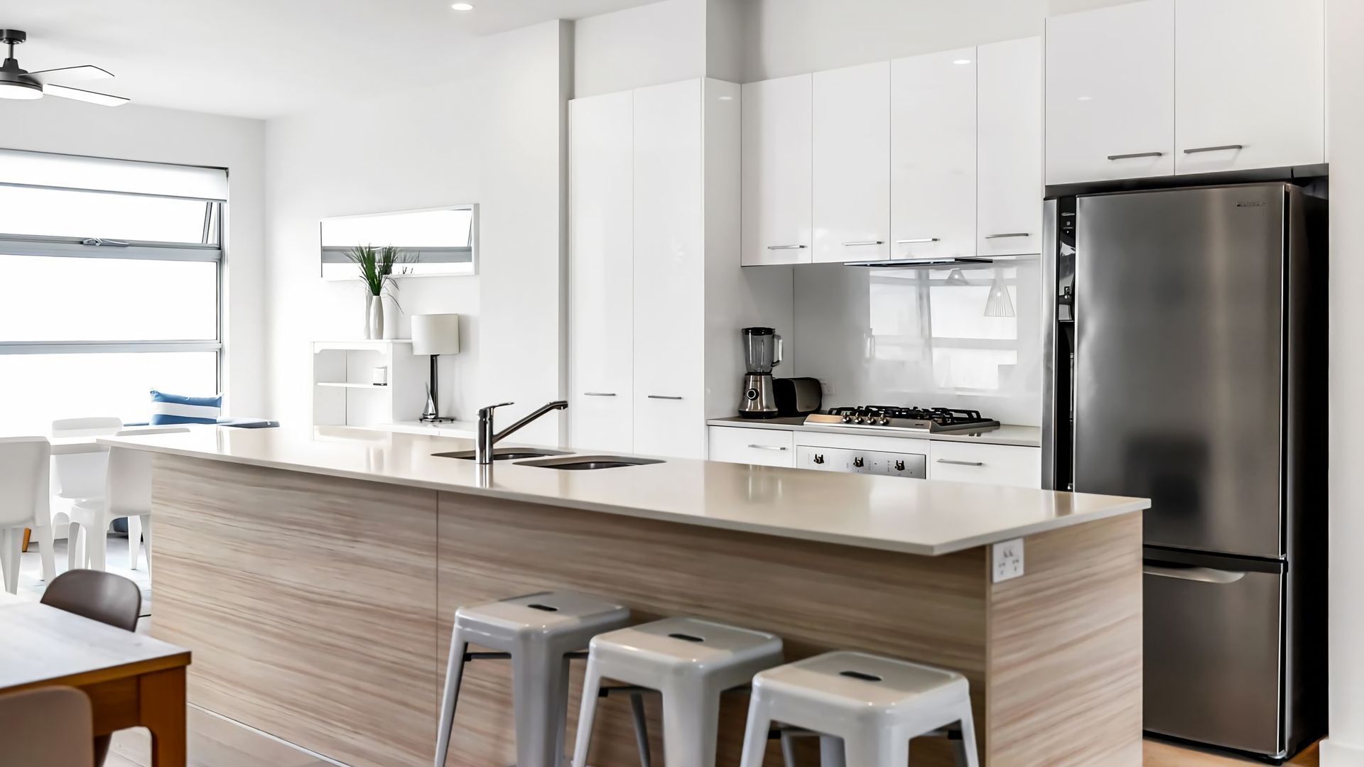 A modern kitchen with white cabinetry, a stainless steel refrigerator, a built-in stove, and a large island with stools.