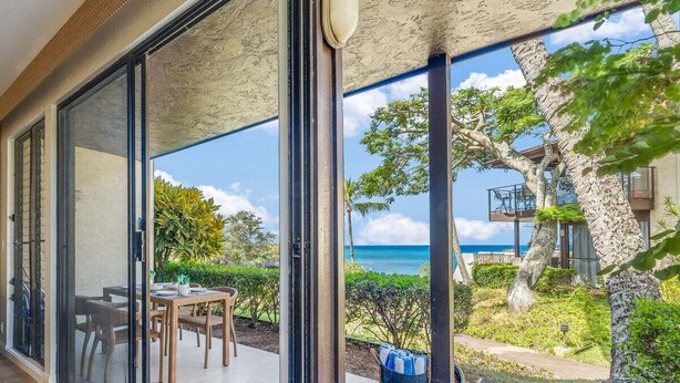 Une villa moderne dotée d’un balcon vitré offrant une vue sur une plage et l’océan.