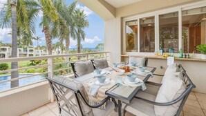 A balcony with a table set for dining, overlooking a pool and palm trees.