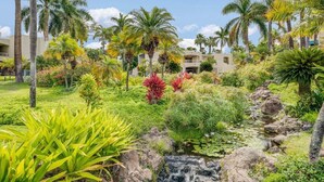 A lush garden with palm trees, a small waterfall, and a building in the background.