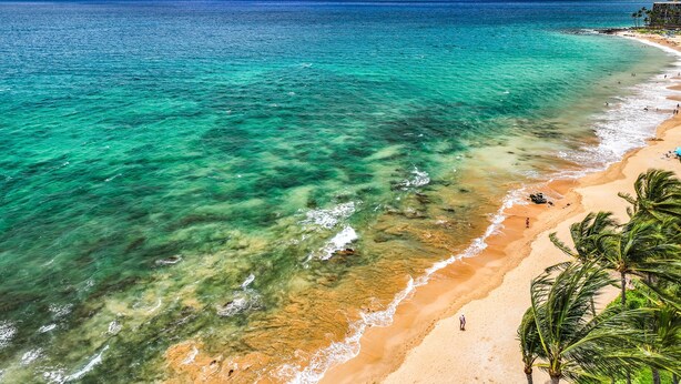 A beach with clear turquoise water, a sandy shore, and a mountain in the distance.