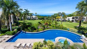 A swimming pool with lounge chairs, surrounded by palm trees and a view of the ocean.