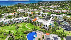 A resort with a swimming pool, palm trees, and a view of the ocean.
