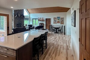 A spacious kitchen with a large island, wooden flooring, and a stone fireplace.