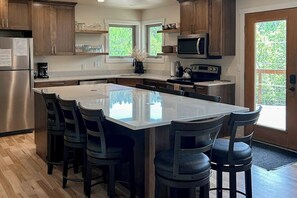 A modern kitchen with a large island, wooden cabinets, and a stainless steel refrigerator.
