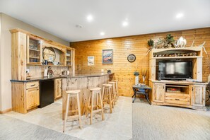 Une cuisine dotée de meubles en bois, un coin bar avec des tabourets, un téléviseur et une étagère décorative ornée de cornes et de figurines.