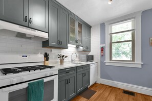 A kitchen with grey cabinets, a white stove, a microwave, and a window with blinds.