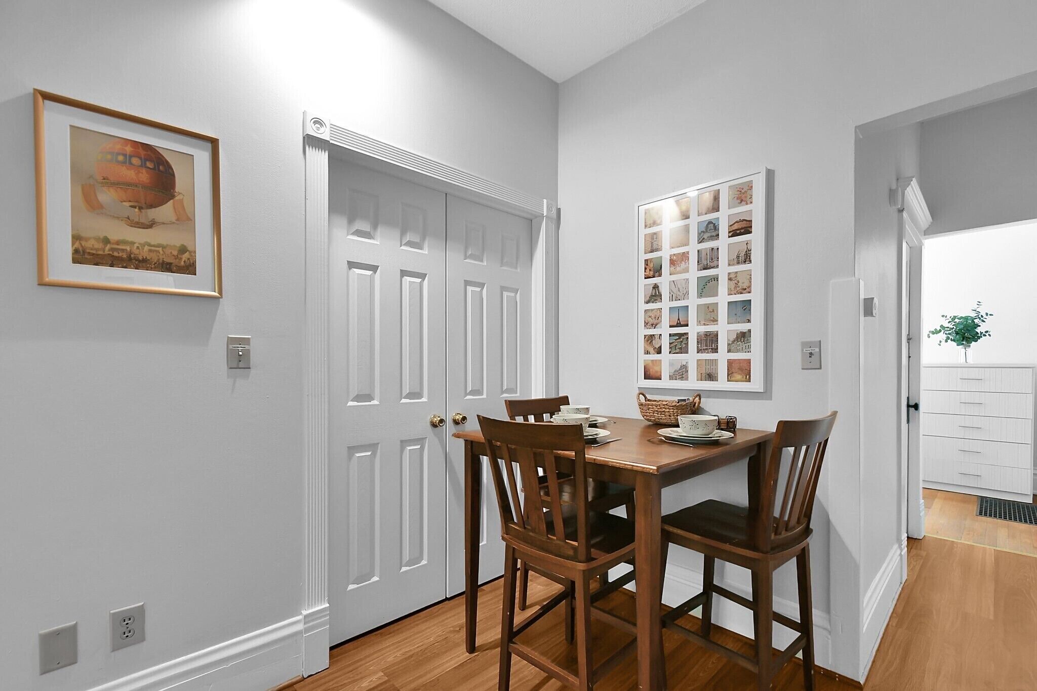 A dining area with a wooden table and chairs, a framed picture on the wall, and a white door.