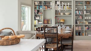 Une bibliothèque spacieuse avec des étagères, un coin repas avec une table et des chaises, et une grande fenêtre.