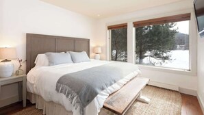 Une chambre à coucher avec un lit, des tables de chevet, une fenêtre donnant sur un beau paysage et un téléviseur à écran plat.