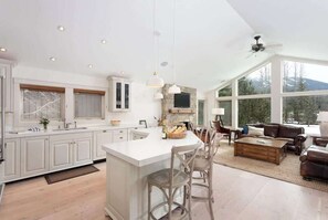 A spacious kitchen with a large island, white cabinetry, and a dining area with a leather couch and wooden coffee table.