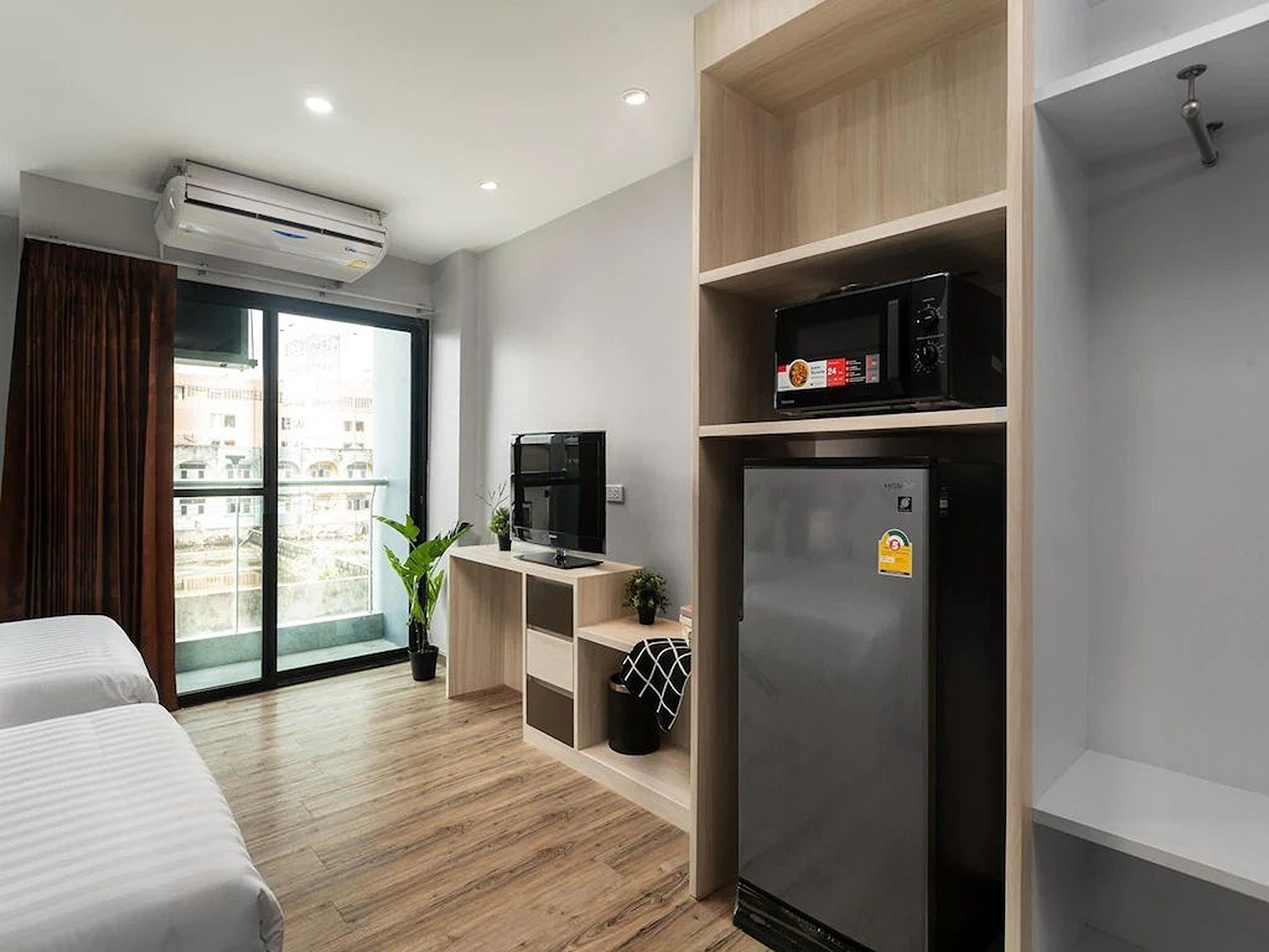 Habitación de hotel moderna con cama, televisión, refrigerador, microondas y ventana con vista a edificios.