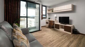 A modern living room with a sofa, a desk, a television, and a sliding glass door leading to a balcony. - VSK RESIDENCE At Suvarnabhumi Airport (Bang Phli)