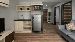A modern apartment with a kitchenette, a grey sofa, and a wooden floor. - VSK RESIDENCE At Suvarnabhumi Airport (Bang Phli)