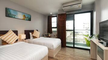 A hotel room with two beds, a TV, an air conditioner, a painting, and a view through the window.