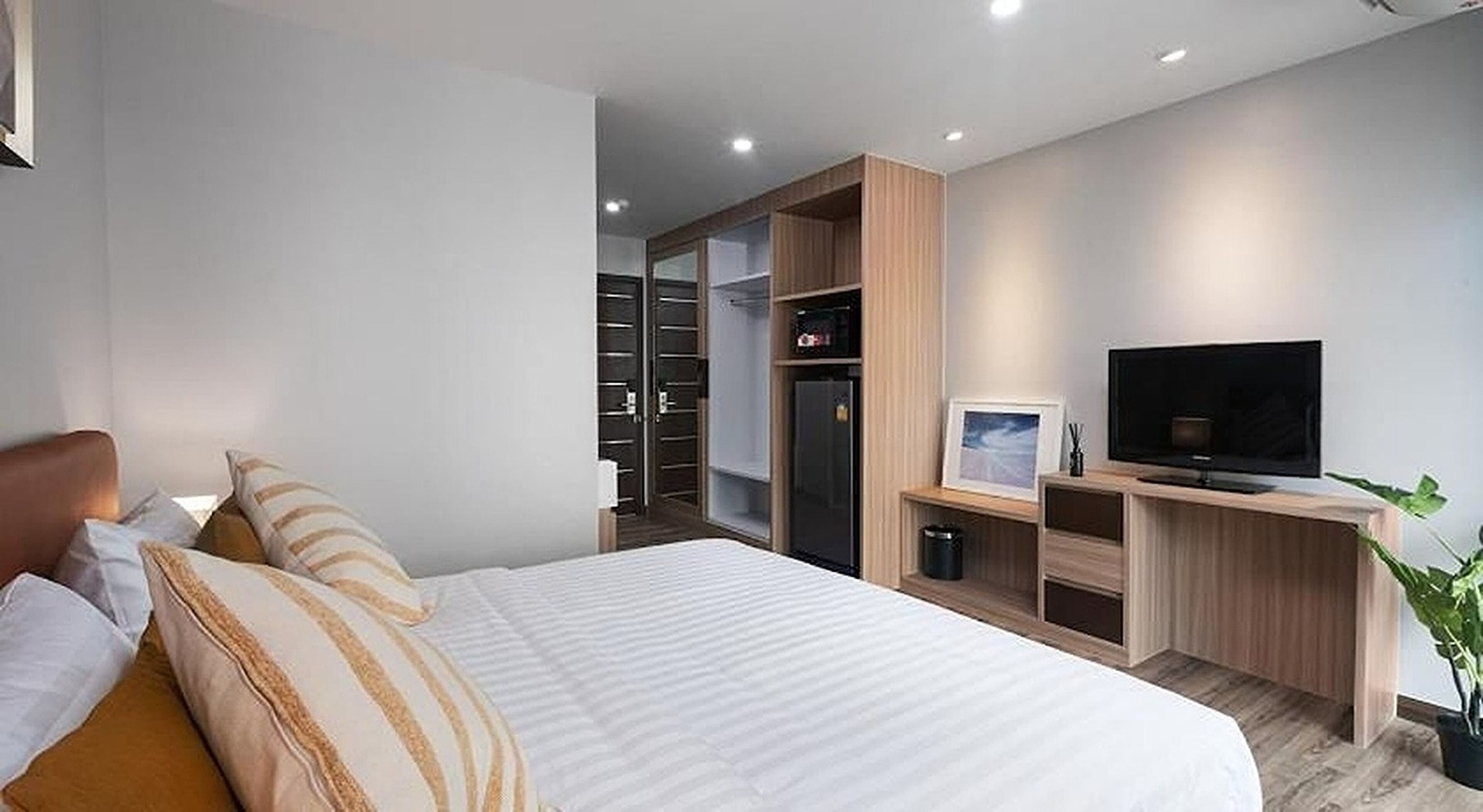 Un dormitorio moderno con cama, televisión, armario y una planta pequeña.