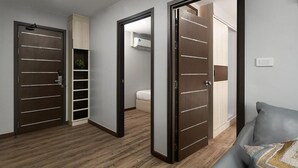 A modern room with a wooden floor, a grey sofa, and a built-in shelving unit. - VSK RESIDENCE At Suvarnabhumi Airport (Bang Phli)